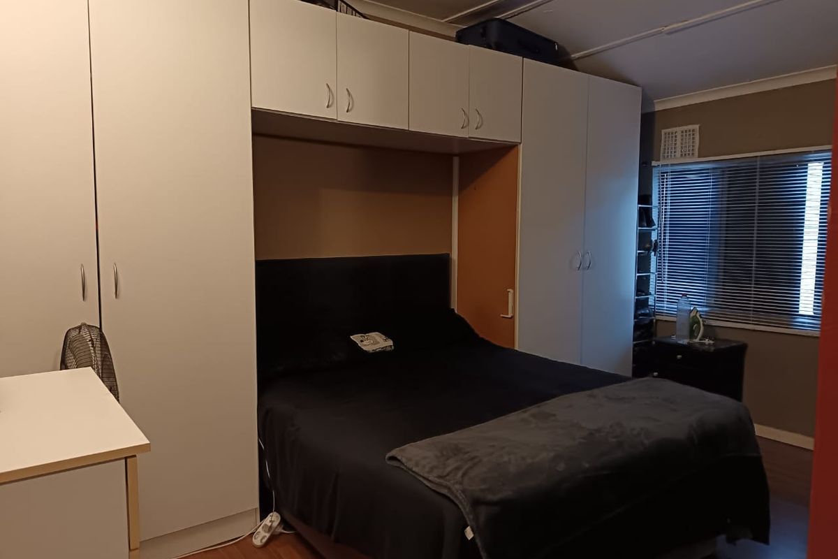 A bedroom featuring extensive built-in white cabinetry surrounding the bed area, laminate flooring, and a window with fitted venetian blinds.