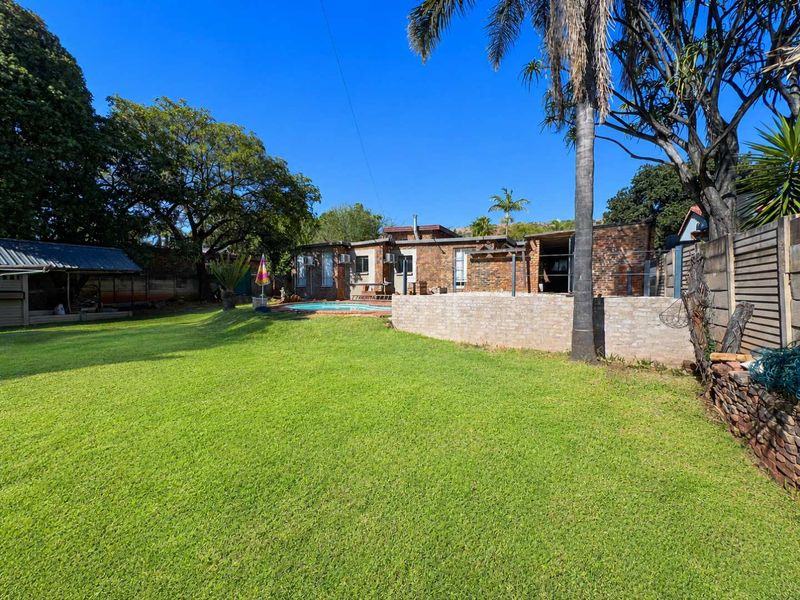 Spacious rear garden featuring a swimming pool, established lawn, mature trees, and an exposed brick house facade.
