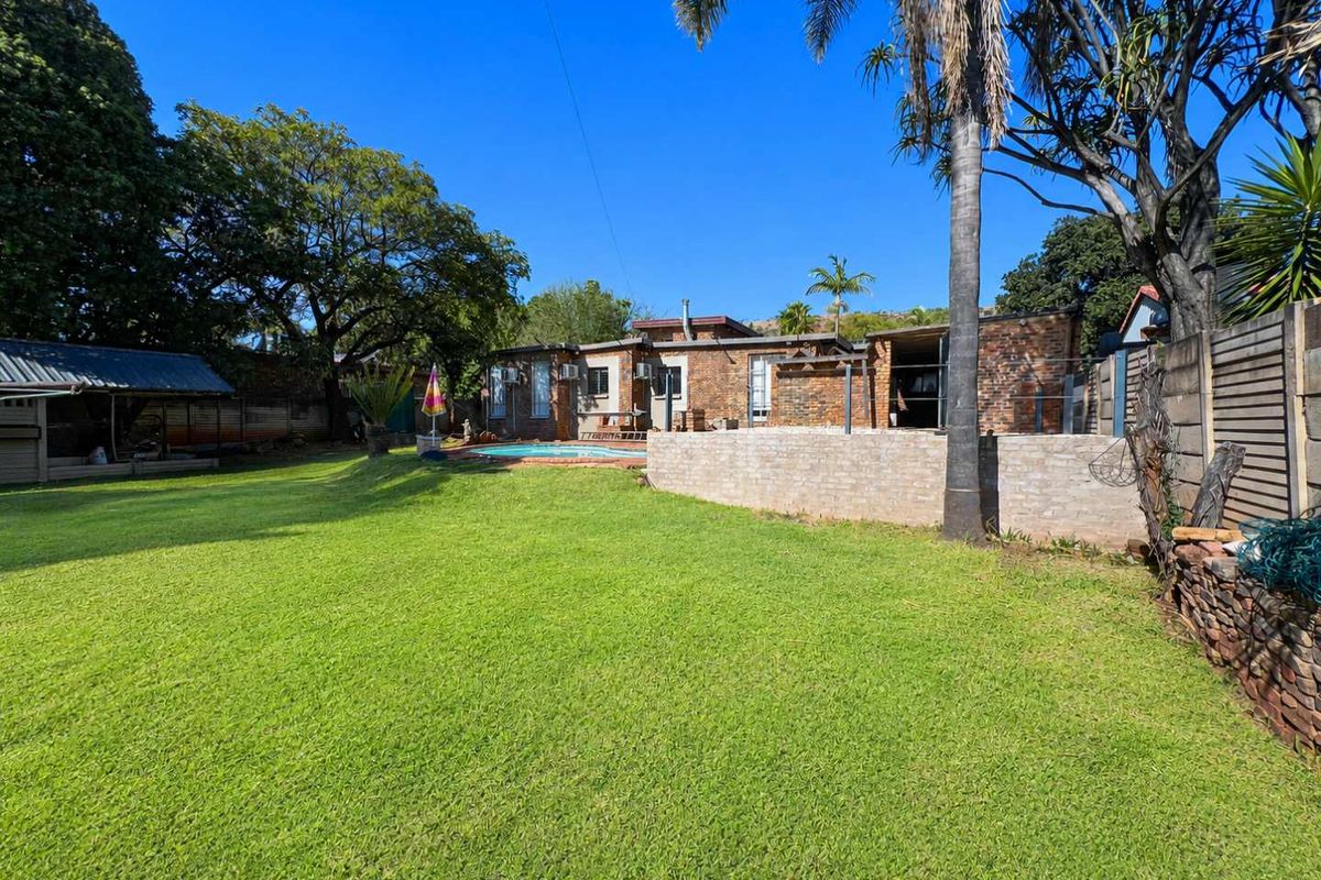 Spacious rear garden featuring a swimming pool, established lawn, mature trees, and an exposed brick house facade.
