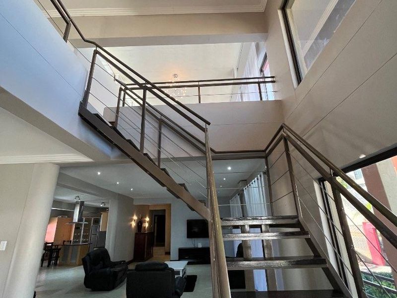 Spacious open-plan living area featuring a modern staircase with stainless steel balustrades, double volume ceilings, and contemporary recessed lighting.