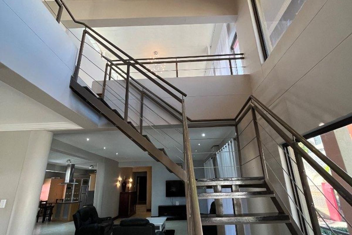 Spacious open-plan living area featuring a modern staircase with stainless steel balustrades, double volume ceilings, and contemporary recessed lighting.