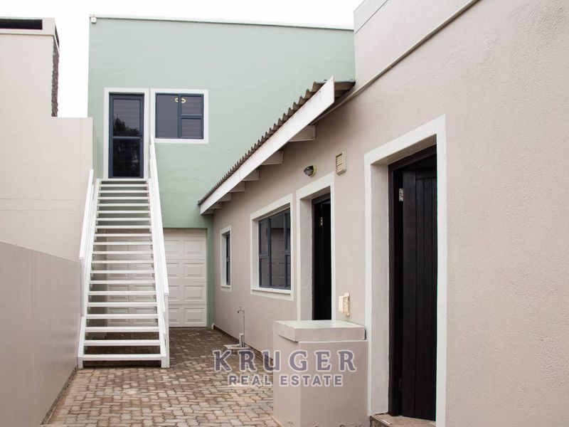 A paved rear courtyard area featuring an external staircase leading to an upper level, with access to a garage and multiple entry points.