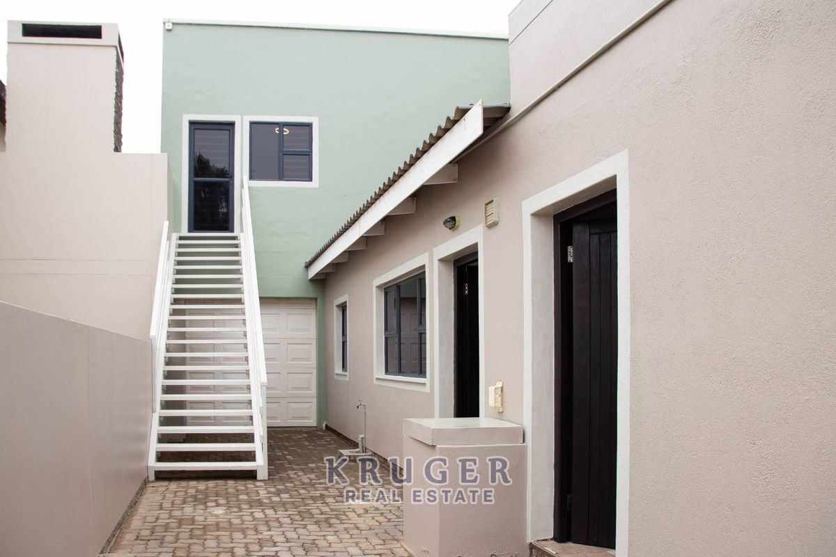 A paved rear courtyard area featuring an external staircase leading to an upper level, with access to a garage and multiple entry points.
