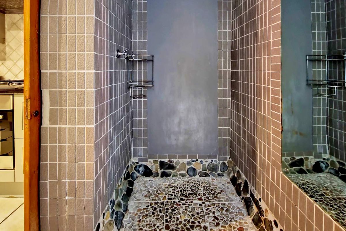 A shower enclosure featuring a pebble-tiled floor, square wall tiles, and a built-in metal shower caddy.