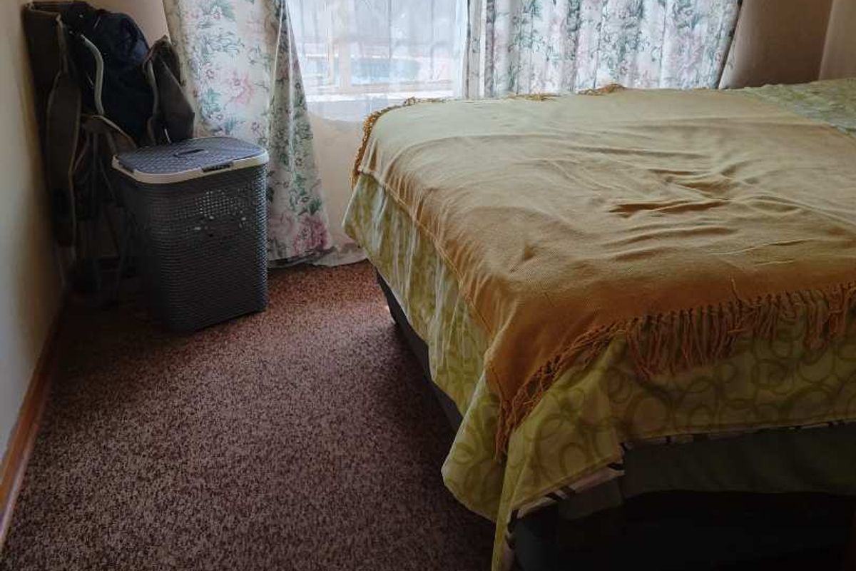A bedroom featuring carpeted flooring and a window with curtains, providing a functional space for rest.