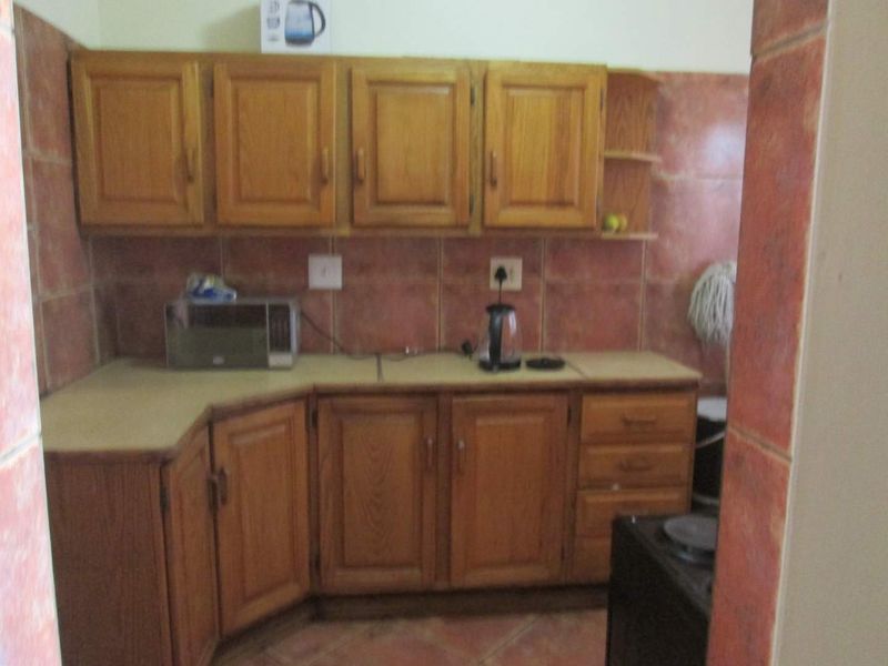 A dated kitchen featuring wooden cabinetry, laminate countertops, and tiled backsplash, offering a functional layout in need of cosmetic updates.