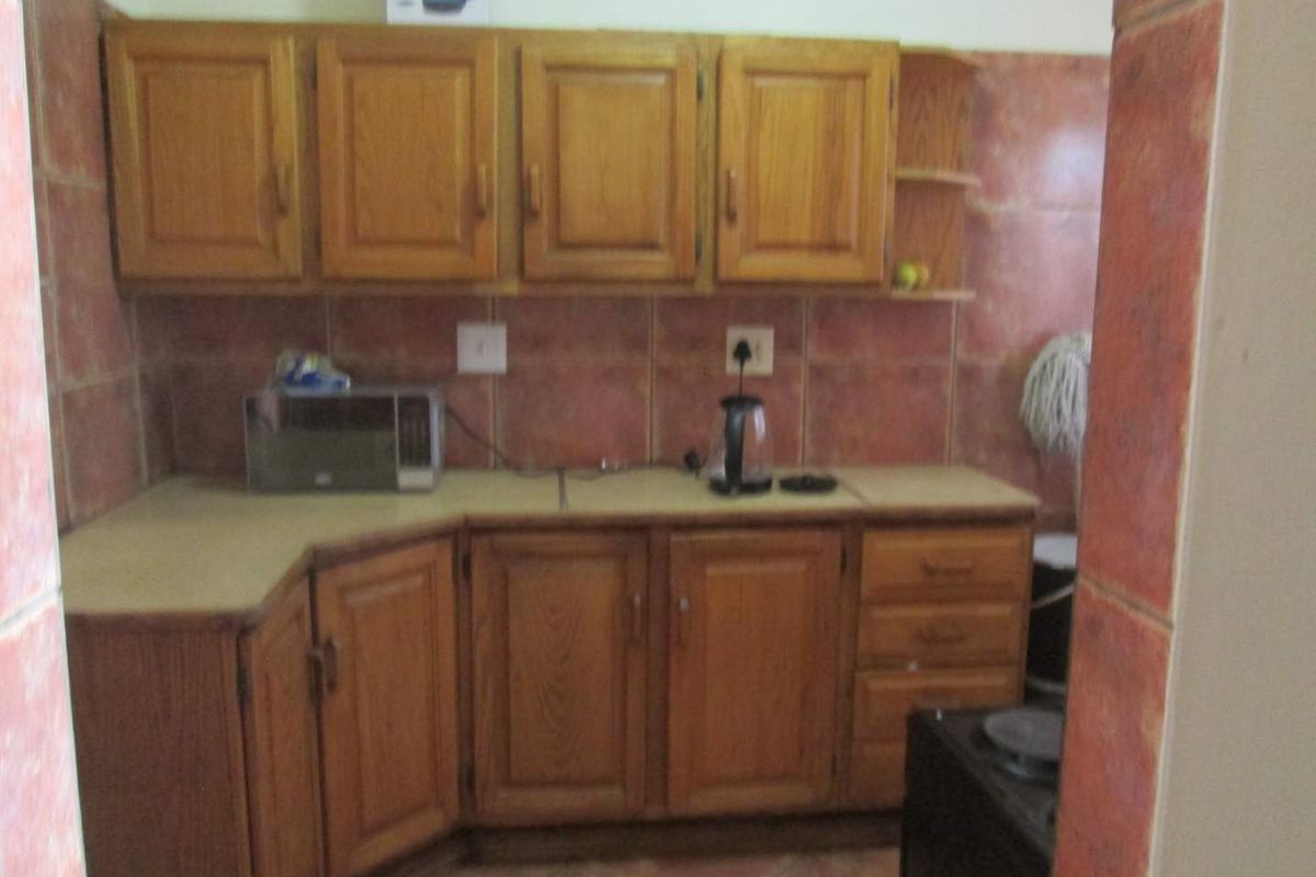 A dated kitchen featuring wooden cabinetry, laminate countertops, and tiled backsplash, offering a functional layout in need of cosmetic updates.