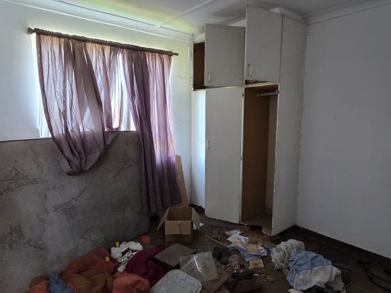 A bedroom featuring a built-in wardrobe and ceiling vent, currently in need of significant renovation and repair to restore its condition.