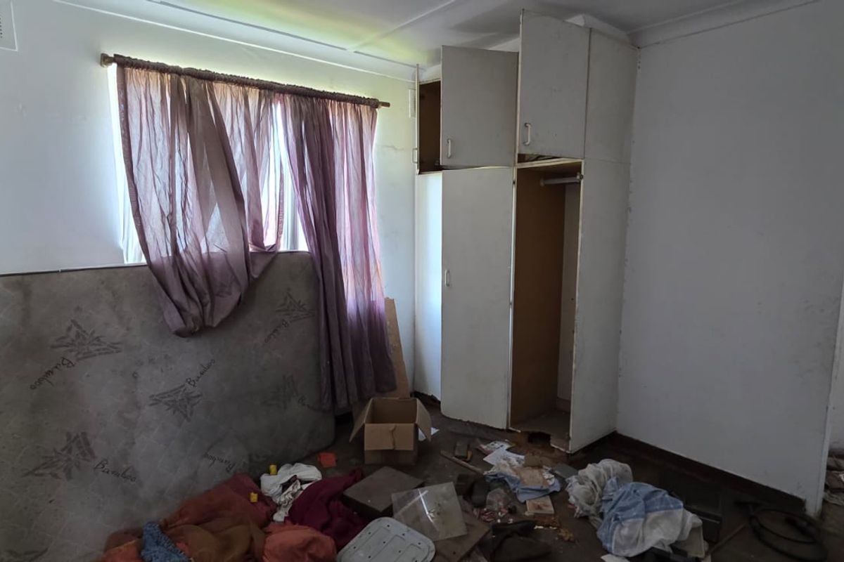 A bedroom featuring a built-in wardrobe and ceiling vent, currently in need of significant renovation and repair to restore its condition.
