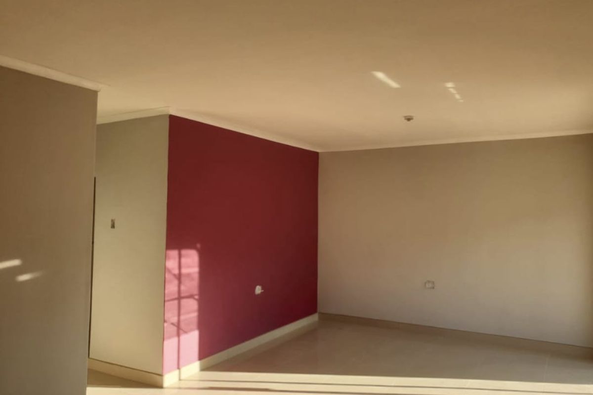 A bright, empty living area featuring neutral and accent-colored walls, tiled flooring, and coving, offering a blank canvas for interior design.