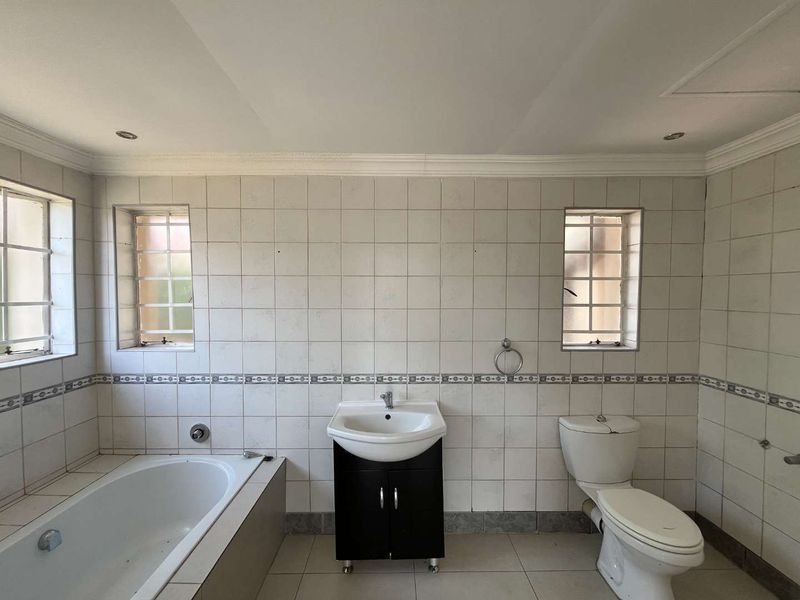 A dated bathroom featuring a built-in bathtub, vanity cabinet, and toilet, finished with tiled walls and flooring. The space is ready for modernization.