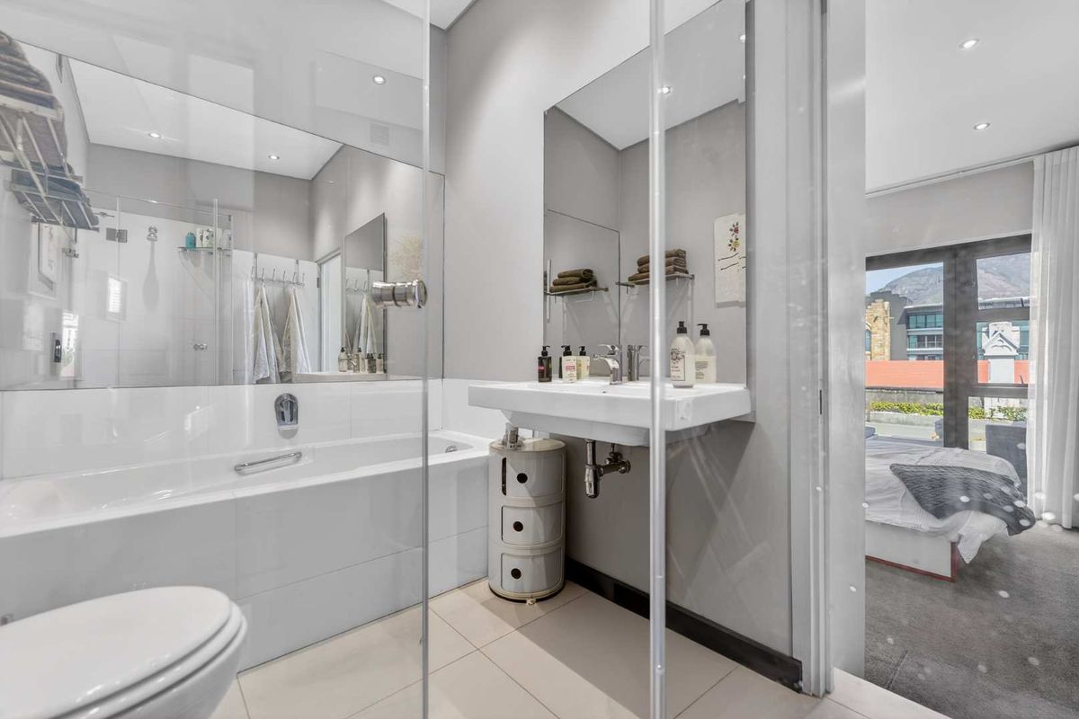 Modern bathroom featuring a wall-mounted basin, built-in bathtub with glass screen, and large mirror, with direct access to the adjacent bedroom.