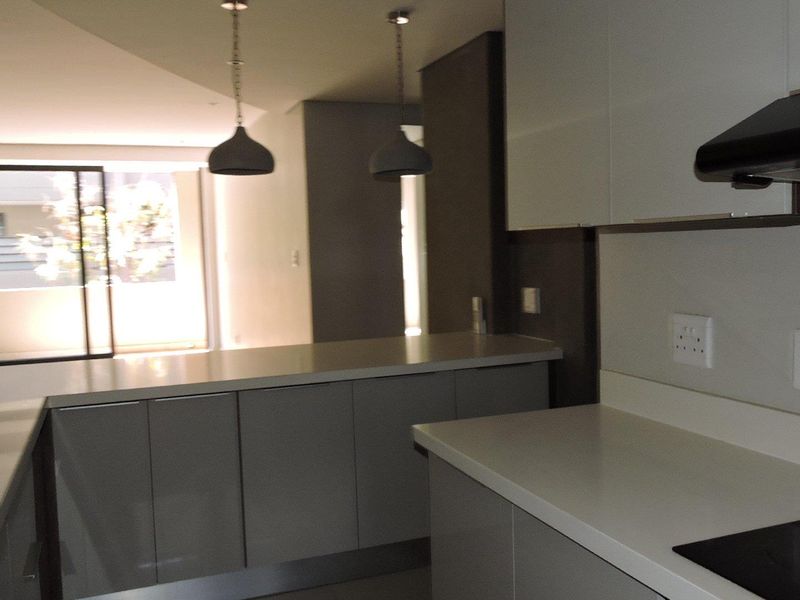 Modern open-plan kitchen featuring sleek cabinetry, stone countertops, and integrated appliances, flowing into a bright living area with access to a balcony.