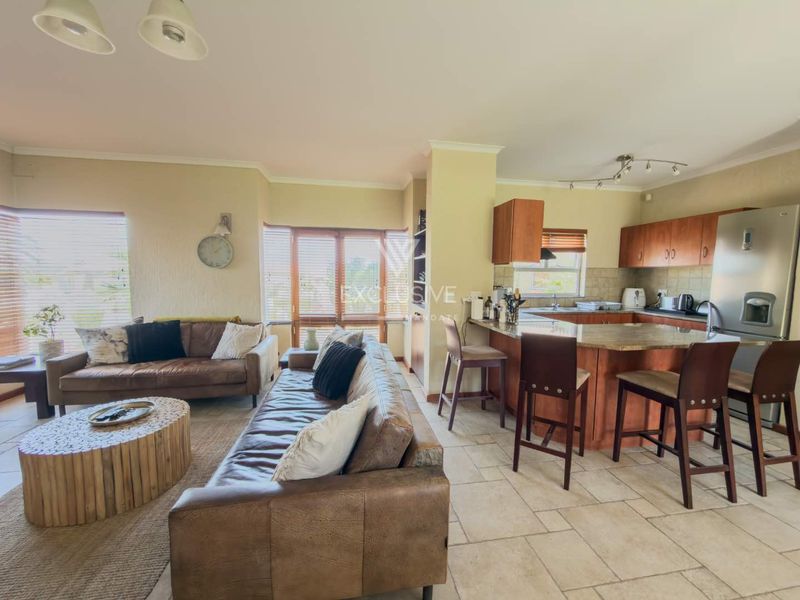 Open-plan living and kitchen area featuring tiled floors, wooden cabinetry, granite countertops, and a breakfast bar, creating a functional and connected living space.