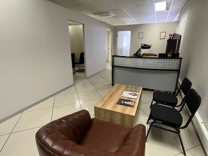 A functional office reception area featuring tiled flooring, a suspended ceiling with recessed lighting, and a built-in reception desk.