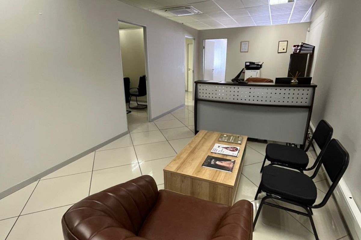 A functional office reception area featuring tiled flooring, a suspended ceiling with recessed lighting, and a built-in reception desk.