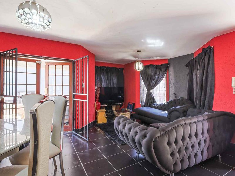 Open plan living and dining area featuring dark tiled flooring, security gate access to the exterior, and bold red wall finishes.