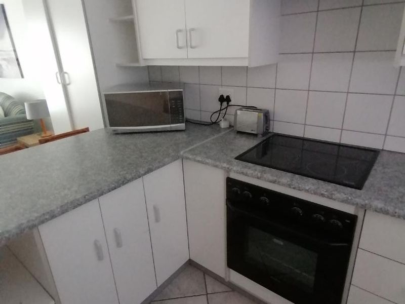 A compact kitchen featuring white cabinetry, grey laminate countertops, a built-in oven with a ceramic hob, and a tiled backsplash.