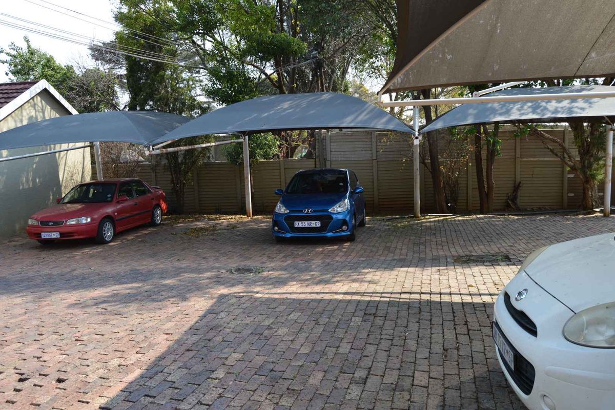 Outdoor parking area featuring paved ground surface and multiple shade-cloth carports for vehicle protection.