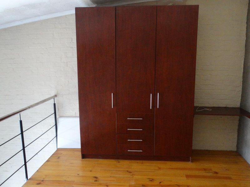 A loft-style bedroom area featuring timber flooring, a built-in dark wood wardrobe, and a metal balustrade overlooking the lower level.