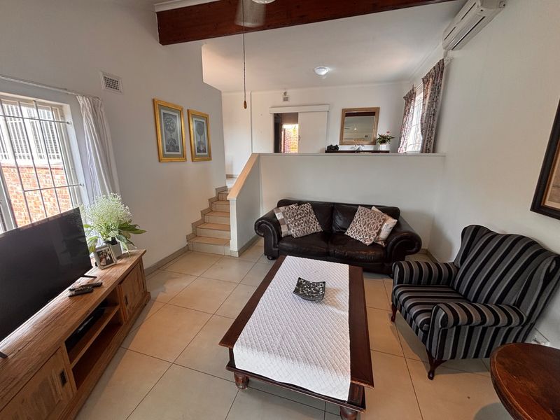 A comfortable living room featuring tiled flooring, an exposed timber ceiling beam, and a split-system air conditioner, with stairs leading to an upper level.