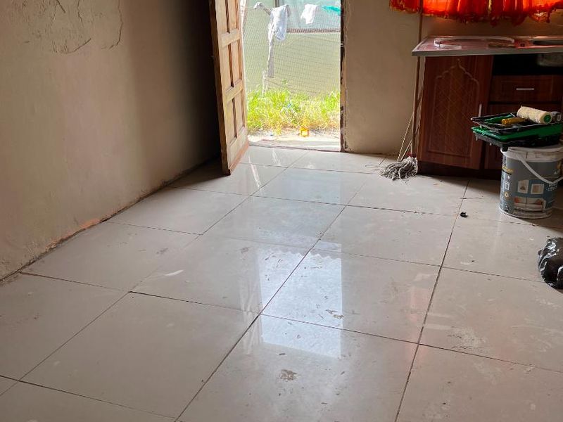 A small, unfinished kitchen area featuring tiled floors, an extractor fan, and basic cabinetry, currently undergoing renovation or maintenance.