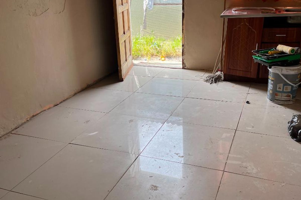 A small, unfinished kitchen area featuring tiled floors, an extractor fan, and basic cabinetry, currently undergoing renovation or maintenance.