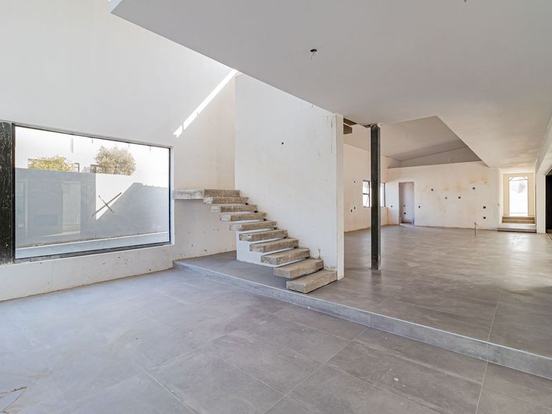 Spacious open-plan living area under construction featuring a modern floating concrete staircase, large format floor tiles, and high vaulted ceilings.