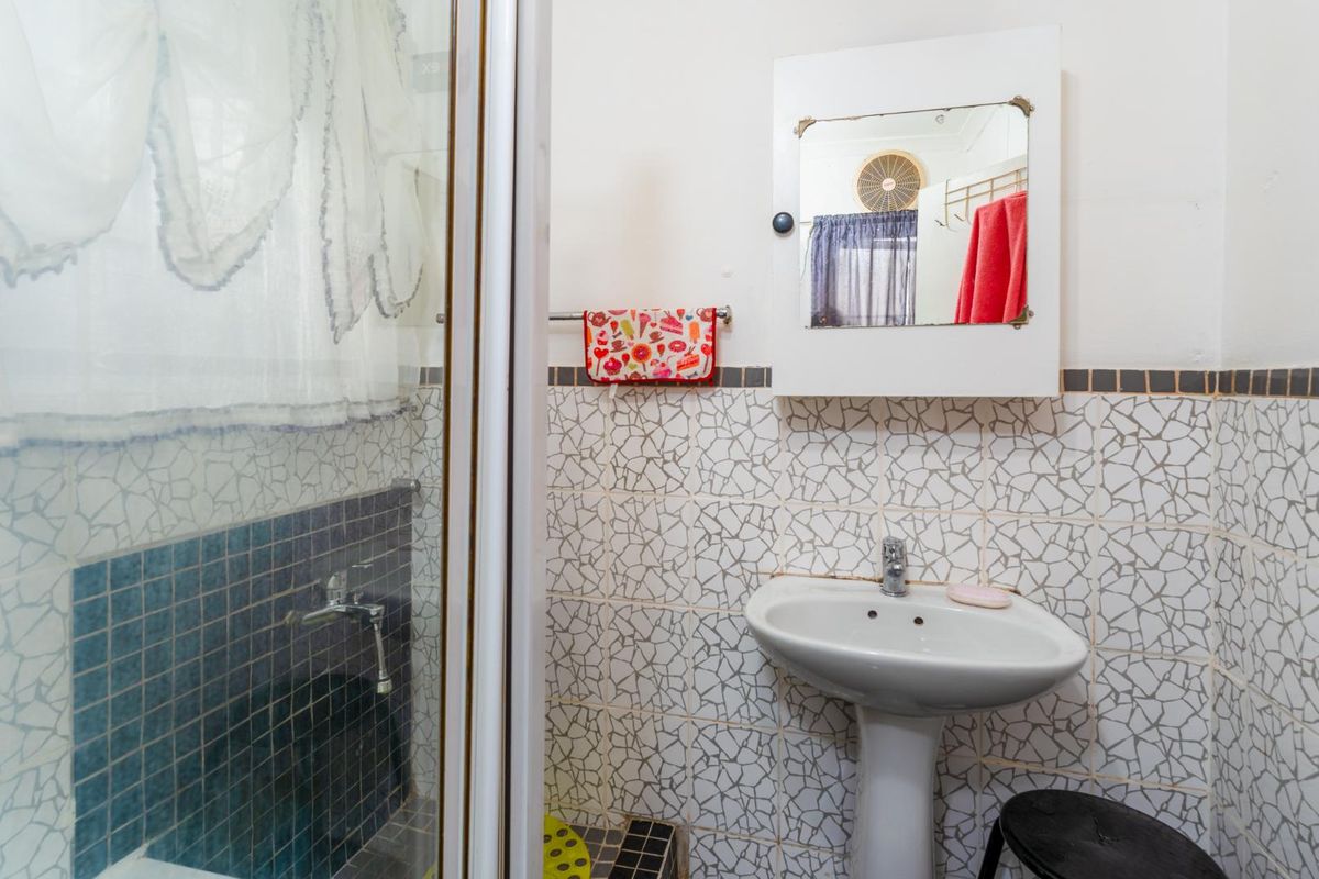 A compact bathroom featuring a pedestal basin, wall-mounted medicine cabinet, and a shower enclosure with mosaic-style wall tiling.