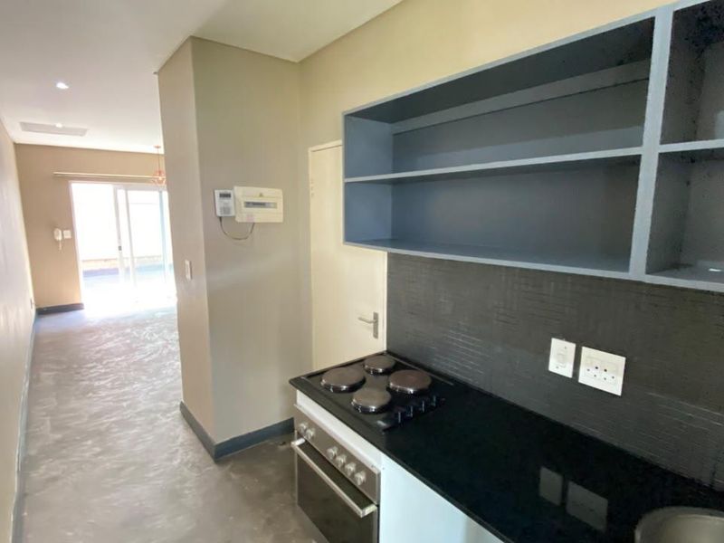 Compact kitchen area featuring built-in oven, electric hob, stone countertops, and open shelving, leading into an open-plan living space.