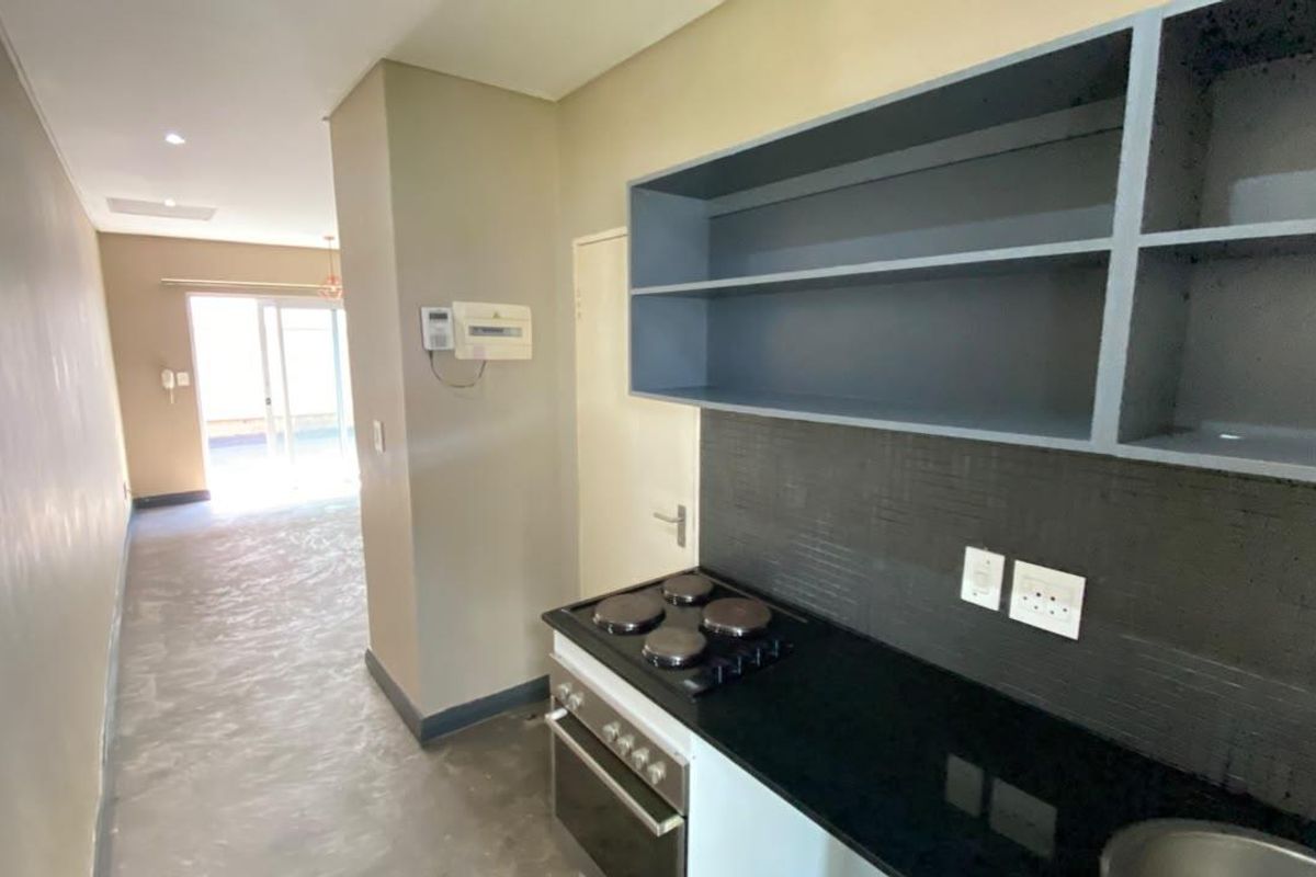 Compact kitchen area featuring built-in oven, electric hob, stone countertops, and open shelving, leading into an open-plan living space.