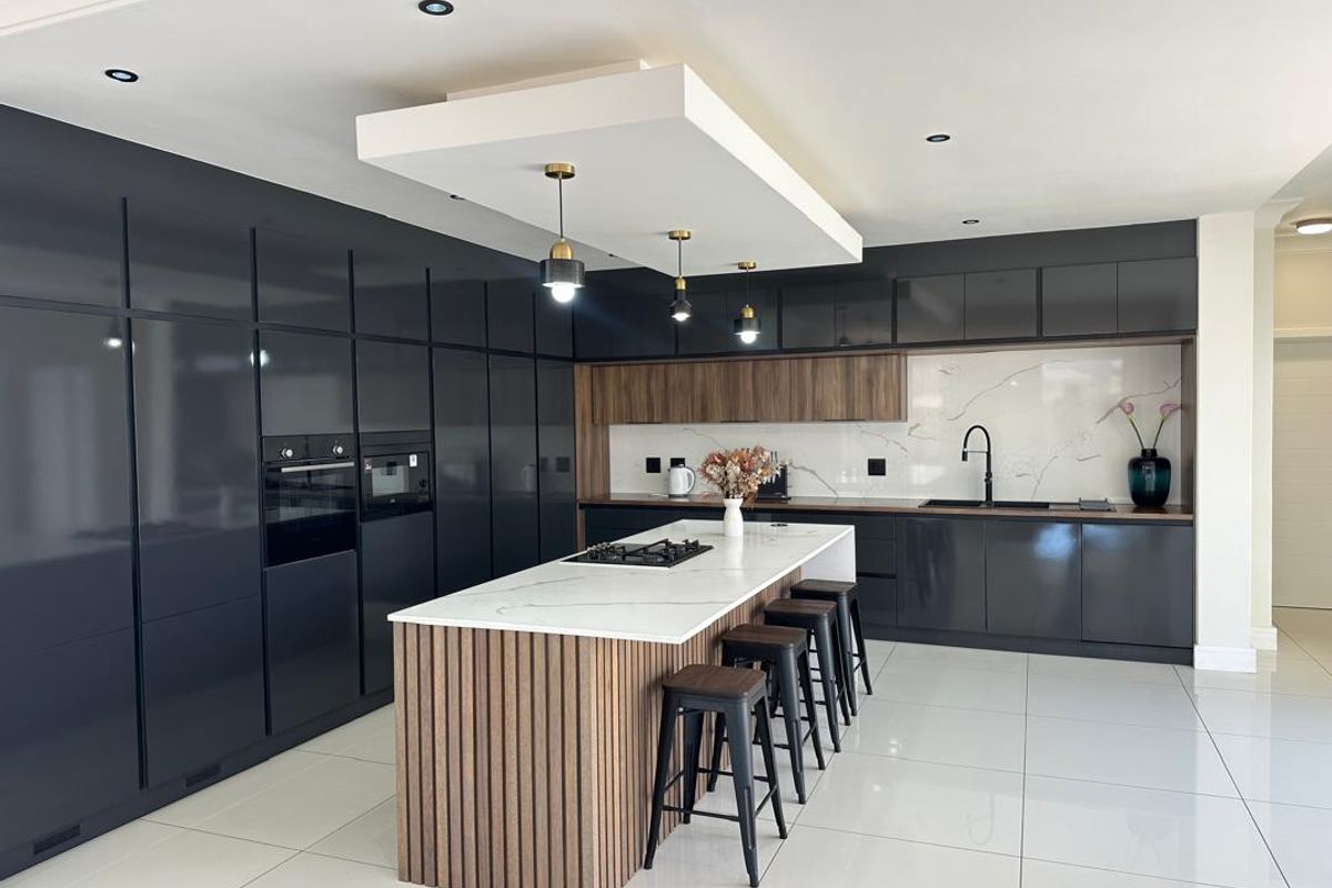 Modern kitchen featuring high-gloss cabinetry, a central island with a stone countertop, integrated appliances, and a sleek marble-look backsplash.