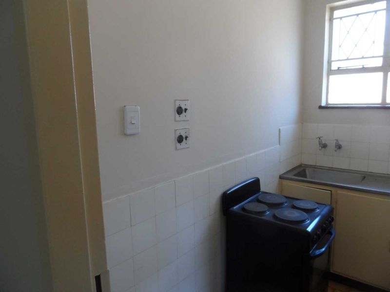 A compact kitchen area featuring a stainless steel sink, tiled splashback, and a freestanding electric stove, offering a functional space ready for modernization.