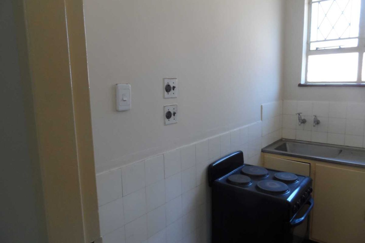 A compact kitchen area featuring a stainless steel sink, tiled splashback, and a freestanding electric stove, offering a functional space ready for modernization.