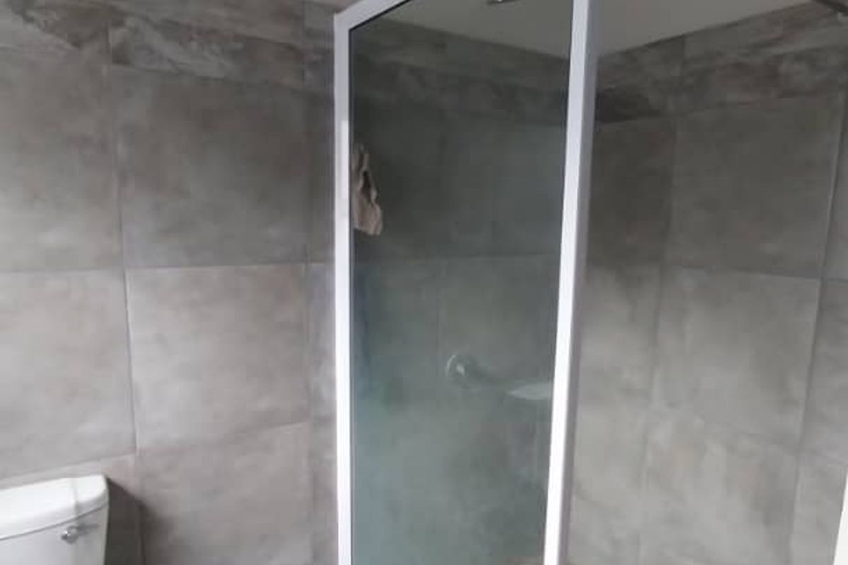 Modern bathroom featuring a walk-in shower with a glass enclosure, pebble-style floor tiling, and a standard white toilet.