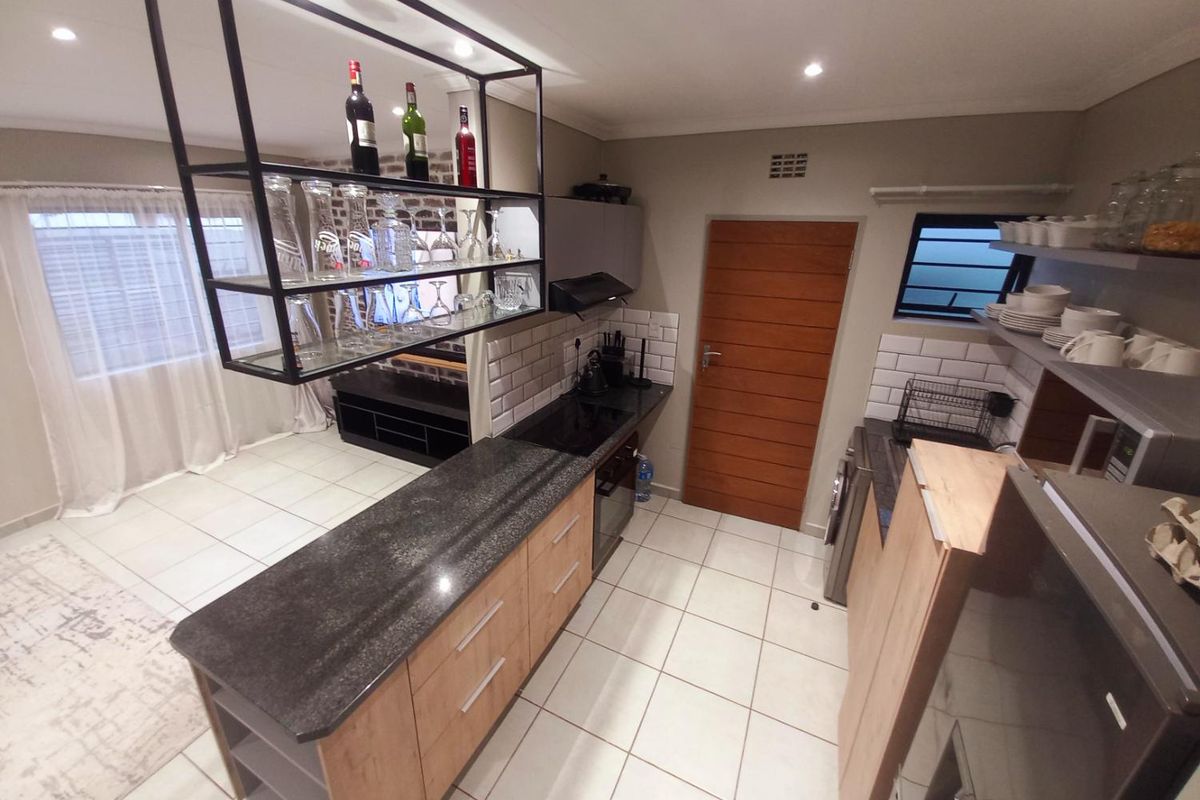 Modern kitchen featuring a central island with stone countertops, built-in cabinetry, subway tile backsplash, and a suspended metal shelving unit.