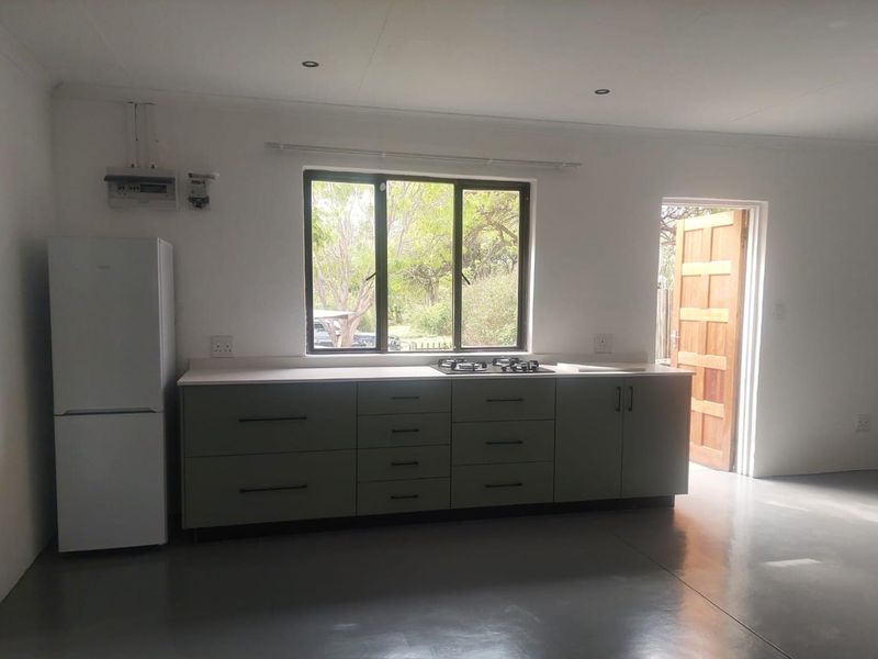 A clean, modern kitchen featuring sage green cabinetry, a gas hob, polished concrete floors, and direct access to the exterior.