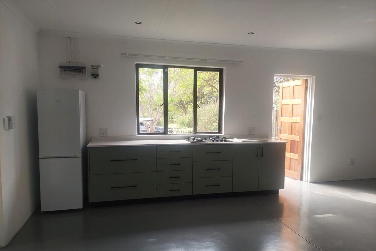 A clean, modern kitchen featuring sage green cabinetry, a gas hob, polished concrete floors, and direct access to the exterior.