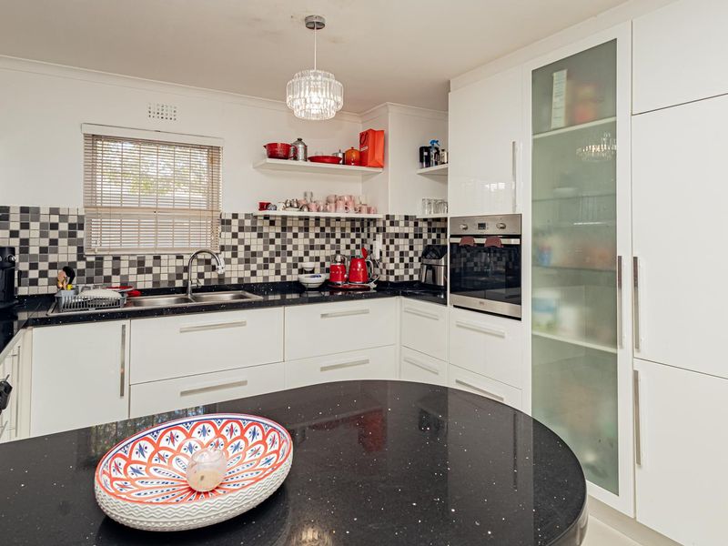 Modern kitchen featuring white cabinetry, black granite countertops, a checkered tile backsplash, built-in oven, gas hob, and a convenient pantry cupboard.