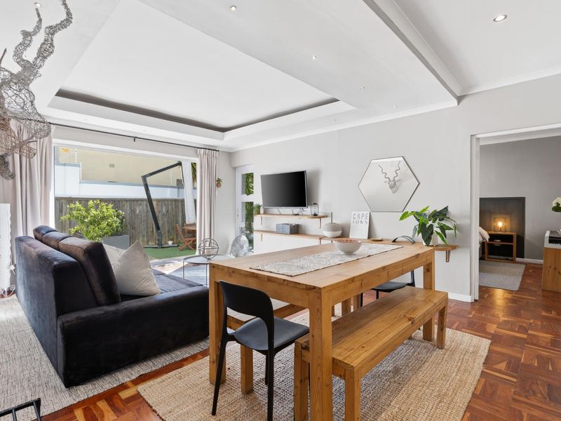 Bright open-plan living and dining area featuring elegant parquet flooring, a recessed ceiling with downlights, and seamless access to the outdoor patio.