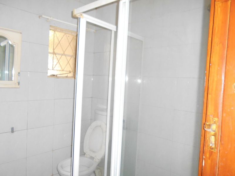 A compact bathroom featuring a shower enclosure, toilet, and tiled walls, requiring cosmetic updates to modernize the space.