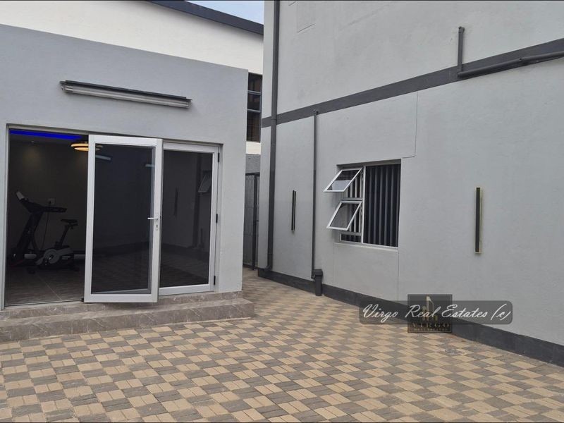 A modern paved rear courtyard featuring clean grey exterior walls, aluminium sliding doors, and secure window fixtures.