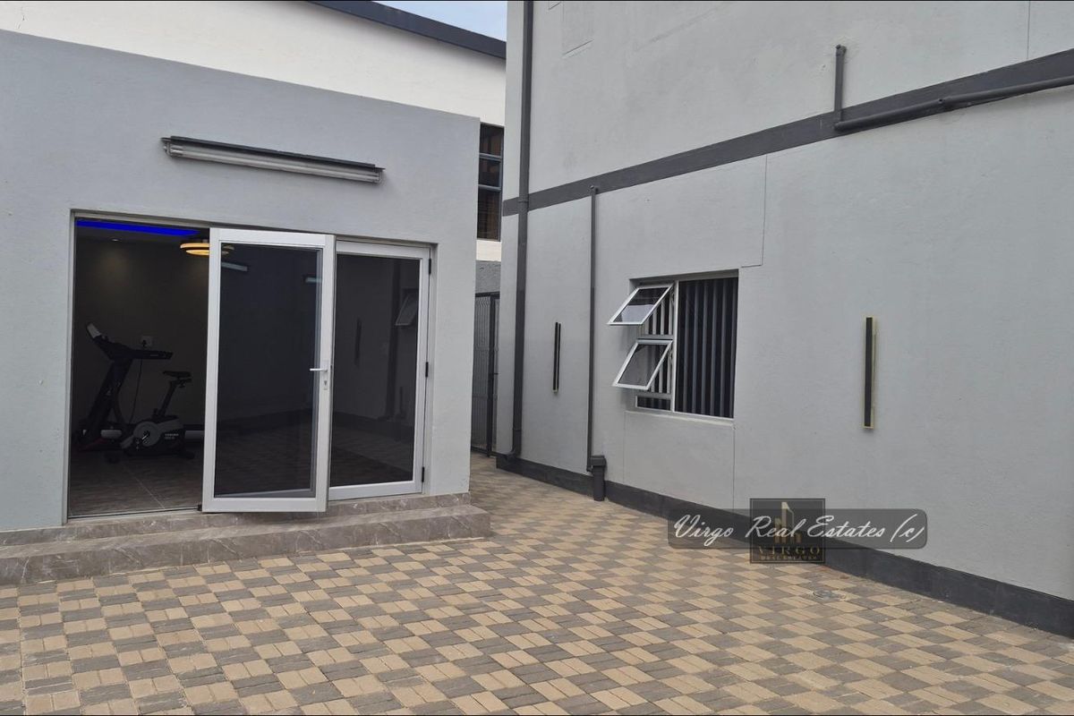A modern paved rear courtyard featuring clean grey exterior walls, aluminium sliding doors, and secure window fixtures.