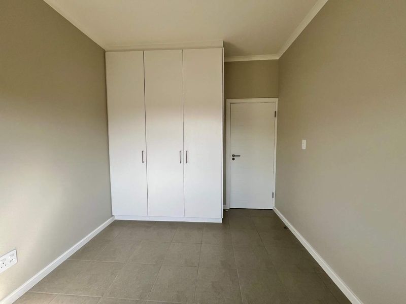 A clean, empty bedroom featuring neutral wall paint, tiled flooring, and built-in white cupboards, providing a versatile space ready for personalization.