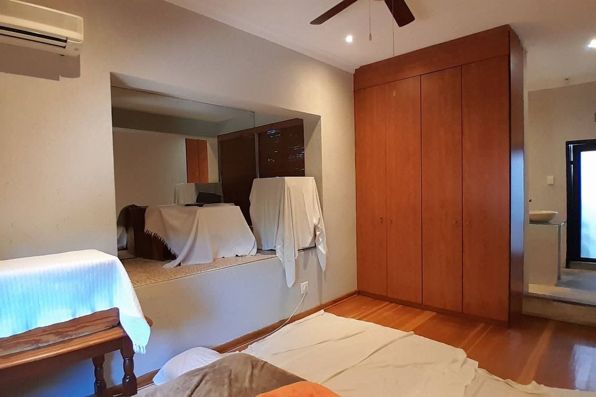 Spacious bedroom featuring built-in wooden cabinetry, a wall-mounted air conditioning unit, and an integrated mirror feature, with direct access to an adjoining bathroom area.