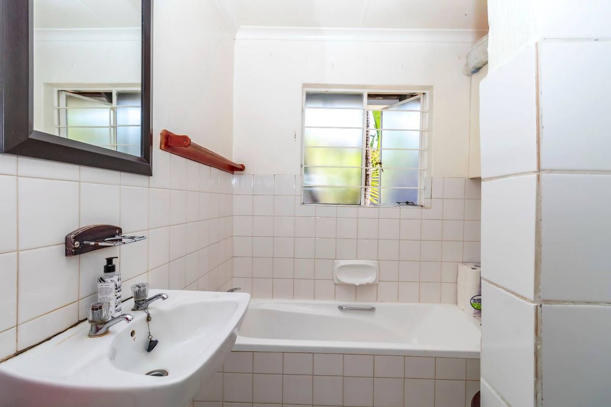 A functional bathroom featuring a built-in bathtub, pedestal basin, and white wall tiling, requiring some cosmetic updates to modernize the space.