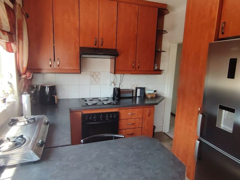 A functional kitchen featuring wood-look laminate cabinetry, dark countertops, a built-in oven, and an electric hob with an extractor fan.