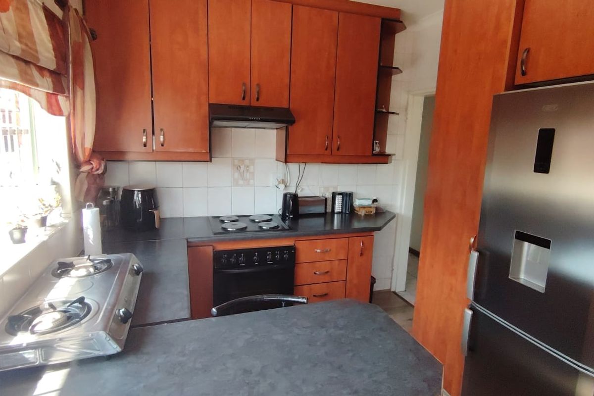 A functional kitchen featuring wood-look laminate cabinetry, dark countertops, a built-in oven, and an electric hob with an extractor fan.