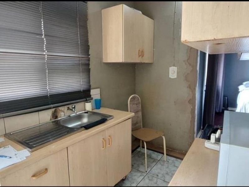 A compact kitchen area featuring built-in cabinetry and a stainless steel sink, currently requiring wall repairs and cosmetic updates to improve functionality and aesthetics.