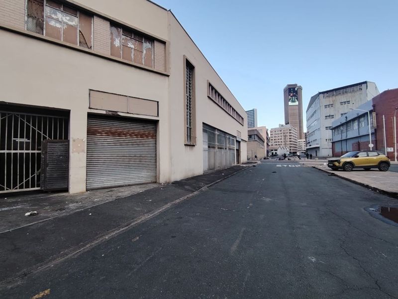 Street-level view of an industrial building featuring roller shutter doors, security grilles, and a weathered facade in an urban setting.